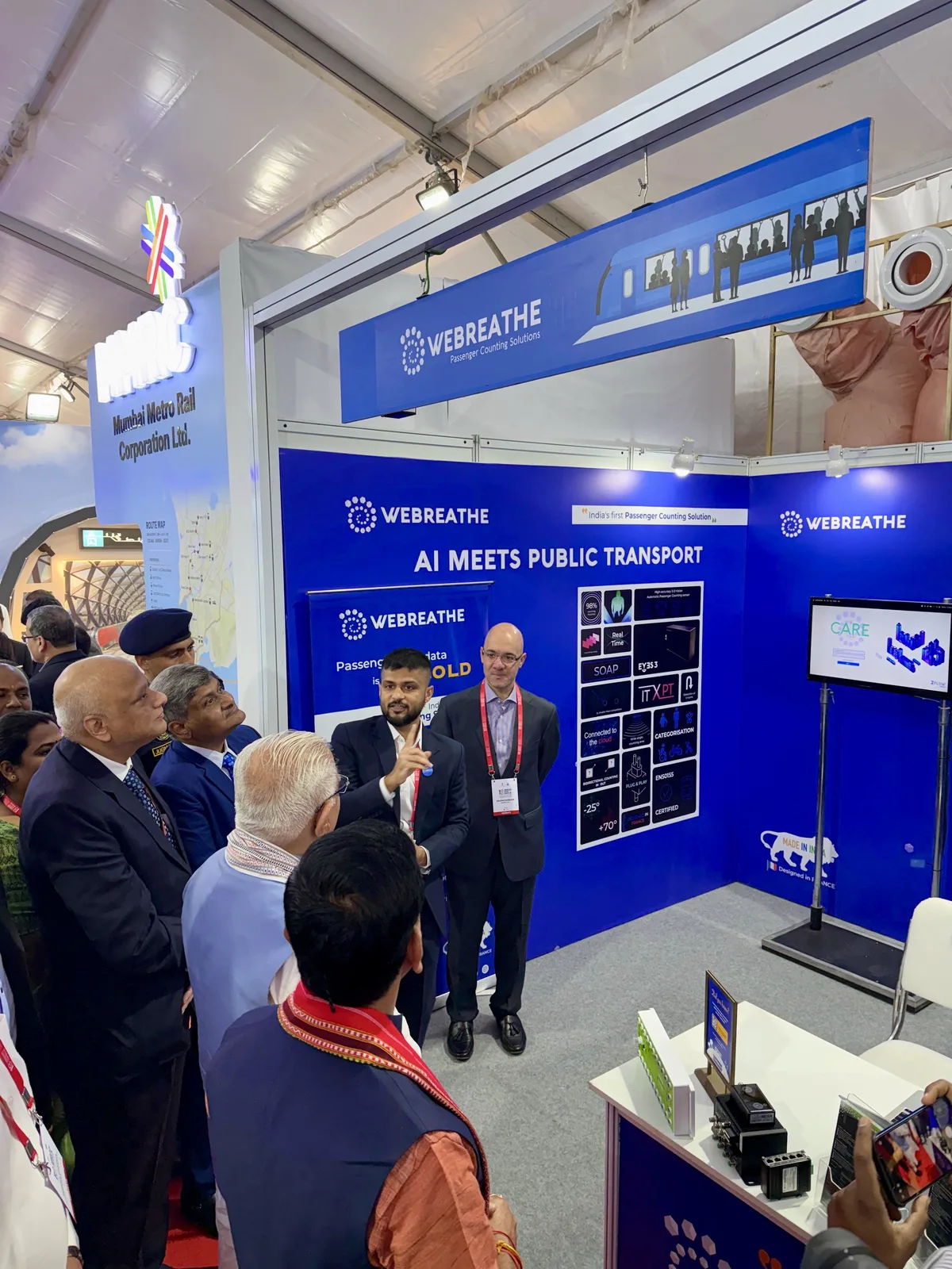 Visitors watching a WEBREATHE presentation beside passenger-counting sensors and a monitor